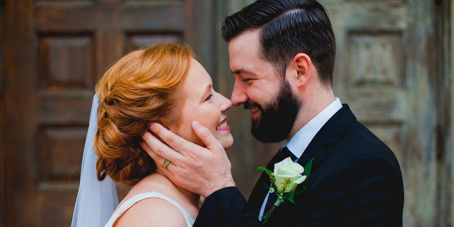 Eine Braut und ein Bräutigam lächeln sich an ihrem Hochzeitstag tief in die Augen, während die Hand des Bräutigams auf der Wange der Braut liegt – als Inspiration für Hochzeitsfoto Ideen aus der ultimativen Hochzeitsfoto-Checkliste.