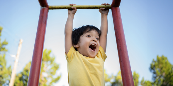 Ein junger Junge lächelt, während er an einem Klettergerüst auf einem Spielplatz hängt, und fängt die letzten Sommertage vor posterXXLs Tipps für ein spaßiges und organisiertes Schuljahr ein.