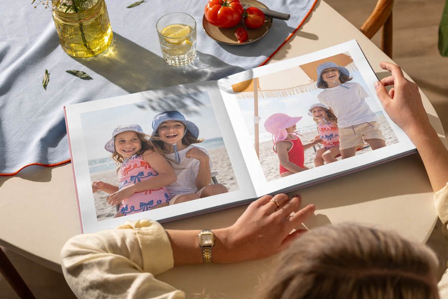 Ein aufgeschlagenes Fotobuch auf einem Küchentisch zeigt Bilder von jungen Mädchen, die am Strand Spaß haben, und veranschaulicht posterXXLs Tipp, mit einem personalisierten Fotobuch auf die Sommererinnerungen zurückzublicken.