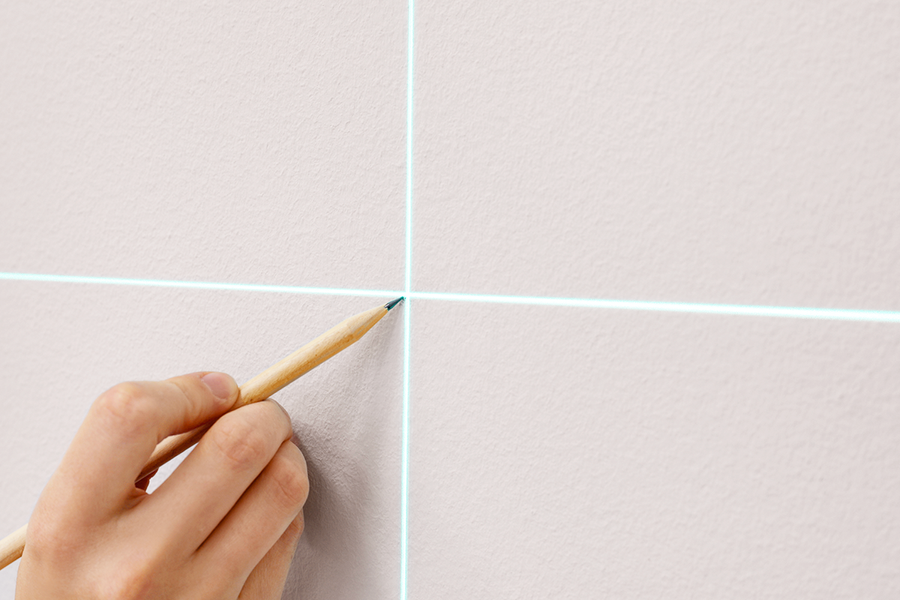 Eine Hand markiert eine Wand zur Vorbereitung des Aufhängens von Wandkunst, und veranschaulicht posterXXLs Schritt-für-Schritt-Tipp, die Wand zu markieren, bevor ein Rahmen-Aufhänge-Set installiert wird.