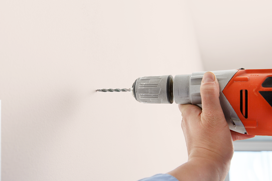 Jemand bohrt in die Wand, und veranschaulicht posterXXLs Schritt-für-Schritt-Tipp, die Hängeschiene mit den mitgelieferten Schrauben und dem Dübel für ein Rahmen-Aufhänge-Set zu installieren.