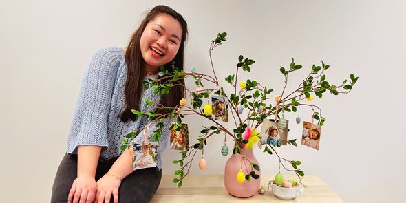 Vannie, Social Marketing Spezialistin bei posterXXL, neben einem fertigen DIY-Oster-Mittelstück, einem Osterbaum in einer Vase mit persönlichen Fotoabzügen an den Zweigen.