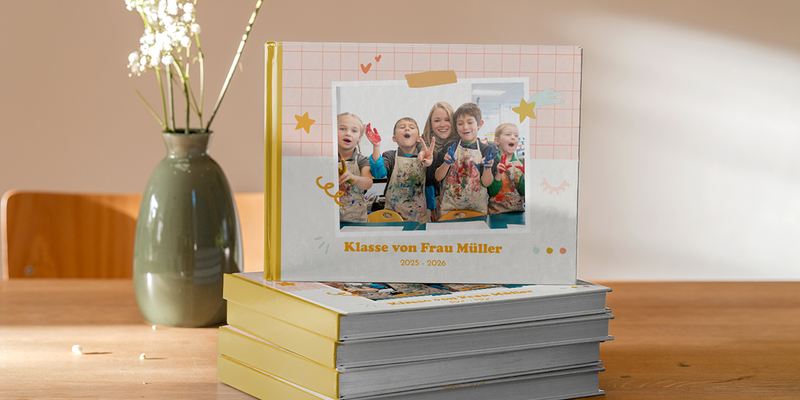 Ein posterxxl Schul-Fotobuch aus dem Jahr 2026 mit lächelnden Kindern im Kunstunterricht – als Inspiration für Schuljahrbücher, Schulfotoalben und Ideen für ein Schul-Fotobuch.