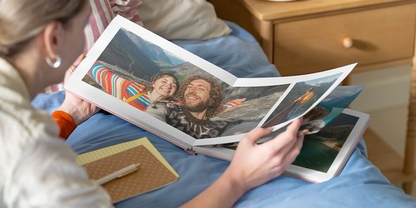 posterxxl Fotobuch Inspiration: Eine Frau betrachtet ein geöffnetes Fotobuch mit einer Doppelseite, auf der ein Paar in einer Berglandschaft zu sehen ist.