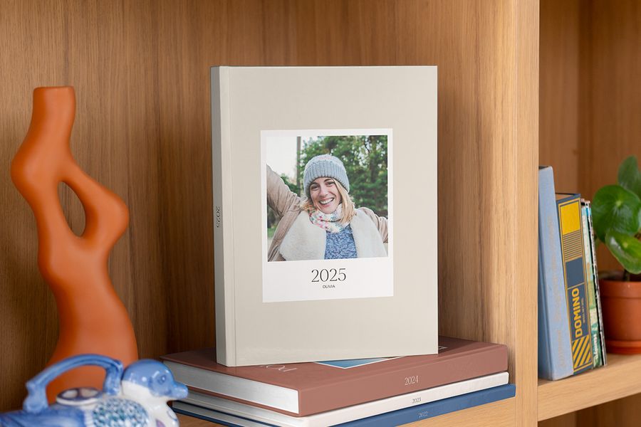 Ein Jahrbuch 2025 mit einer lächelnden Frau auf dem Cover und darunter gestapelten Jahrbüchern aus den Vorjahren.