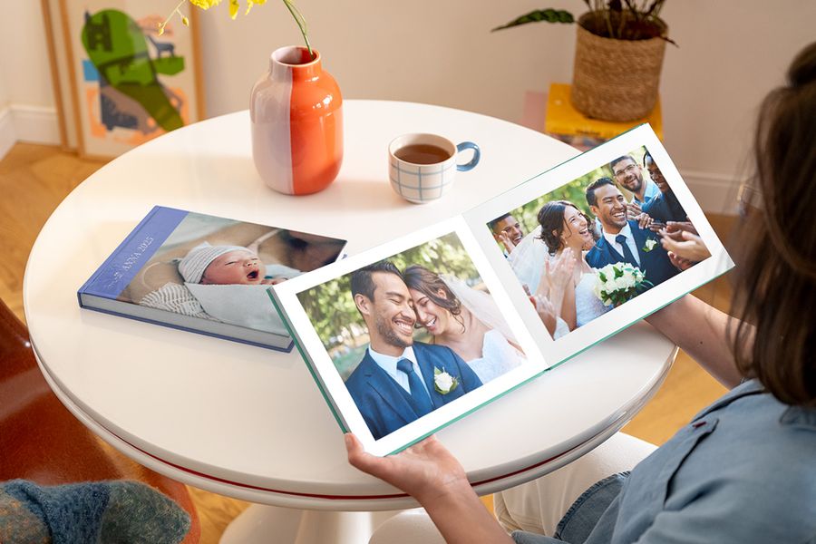 Eine Frau blättert in einem Foto-Jahrbuch mit Hochzeitsfotos; daneben liegt ein weiteres Fotobuch auf dem Tisch, das ein Baby zeigt.