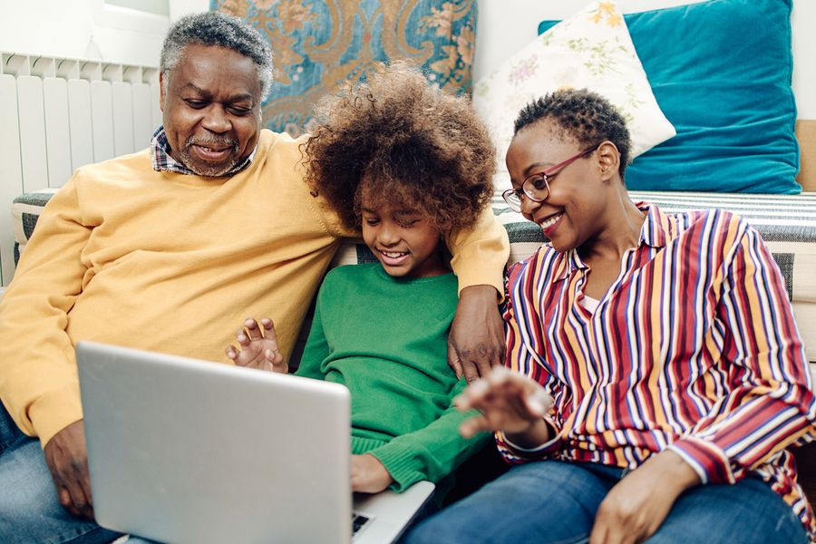 Eltern und Kind lächeln, während sie sich um einen Laptop versammeln, um gemeinsam ein PosterXXL-Jahrbuch zu erstellen.