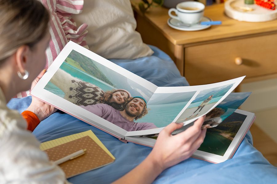 Eine junge Frau betrachtet ein Foto-Jahrbuch, das auf einer Seite mit einem Reisefoto aufgeschlagen ist.