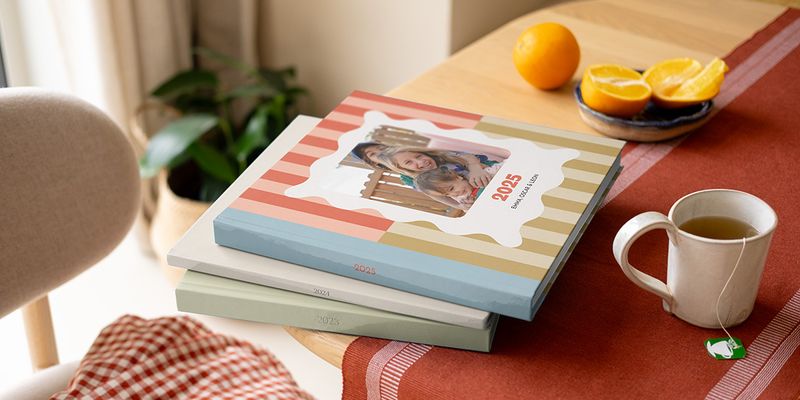 Ein Stapel bunter Fotojahrbücher und Fotobuch Jahrbücher von PosterXXL mit verschiedenen Mustern auf einem Couchtisch.