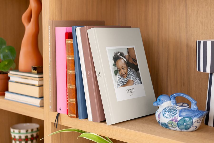 Eine Reihe bunter Jahrbuch Fotobücher und Fotobuch Jahr von PosterXXL, ordentlich in einem Regal ausgestellt.