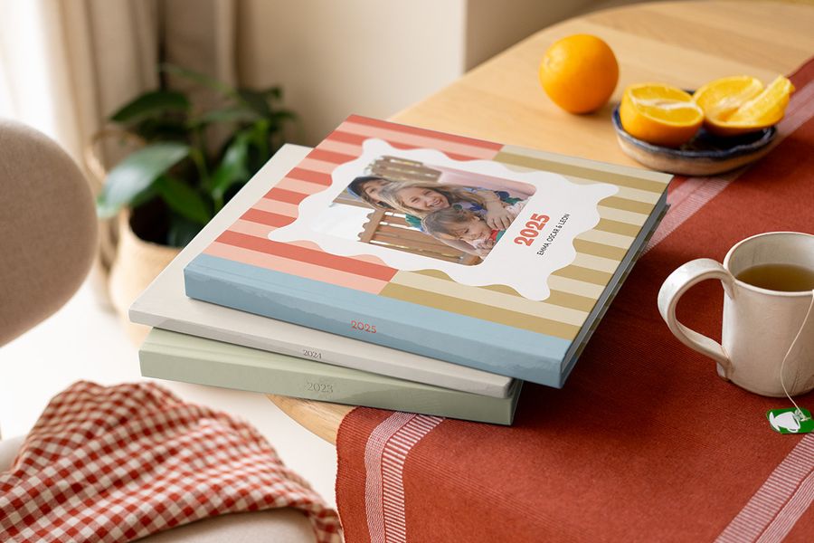 Ein Stapel bunter Fotojahrbücher und Fotobuch Jahrbücher von PosterXXL mit verschiedenen Mustern auf einem Couchtisch.