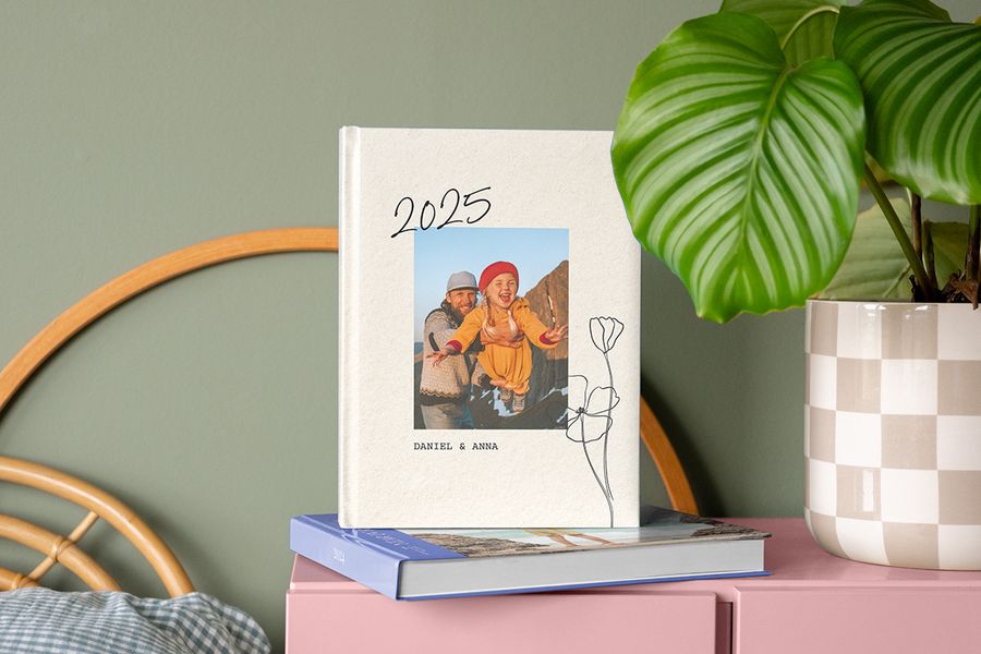 Ein Jahrbuch Fotobuch 2025 mit einem Vater-Tochter-Bild auf dem Cover, ruhend auf dem Jahres Fotobuch von 2024 auf einem Nachttisch.