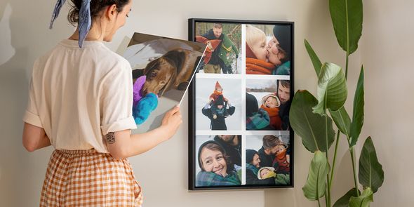 Personalisierte Wandbilder Ideen von posterXXL: Eine Frau betrachtet eine gerahmte Fotocollage mit Familienbildern.