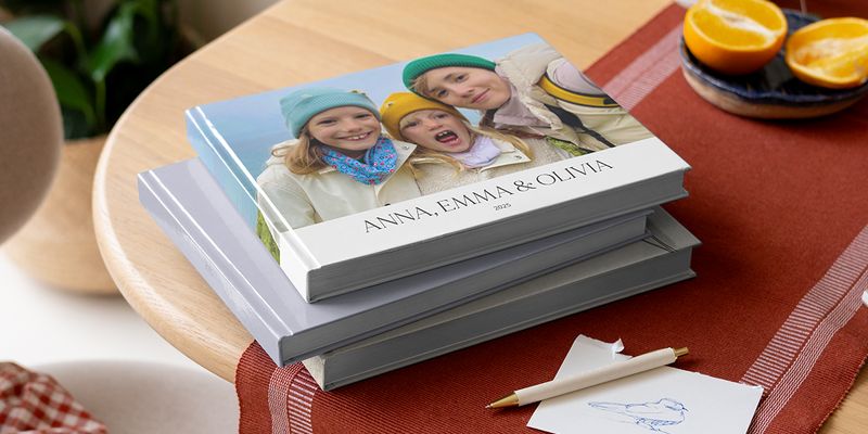 Eine Auswahl an Fotobüchern von posterXXL auf einem Tisch mit einem Stift, die Geschwister auf dem Cover zeigen als Inspiration für sprüche für ein fotobuch.