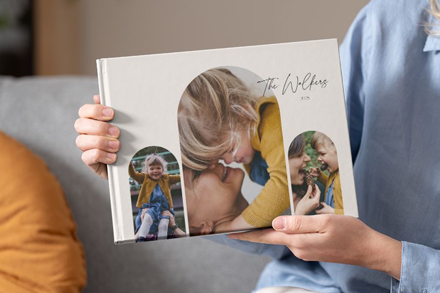 Jemand hält ein Familien-Fotobuch mit mehreren Bildern auf dem Cover, ideal für fotobuch sprüche familie und sprüche für fotobuch familie.