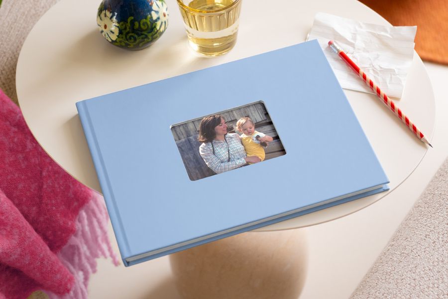 Ein blaues posterXXL Fotobuch mit Fenstercover, auf dessen Vorderseite eine Frau mit ihrem Baby zu sehen ist – als Inspiration für ein Fotobuch zum Muttertag und ein persönliches Muttertagsgeschenk.