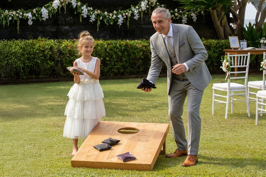Ein junges Mädchen in festlicher Hochzeitskleidung und ein älterer Mann im Anzug spielen Hochzeit-Cornhole und werfen Säckchen in das Brett – als Inspiration für posterXXL Hochzeitsspiele im Freien und Hochzeitsspiele für Gäste.