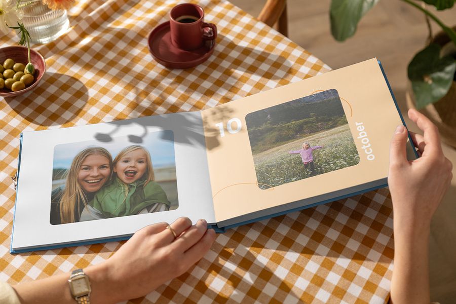 Ein geöffnetes posterXXL Coffee Table Fotobuch mit einer Mutter und ihrer Tochter auf der einen Seite und einem kleinen Mädchen, das über ein Blumenfeld läuft, auf der anderen – als Inspiration für ein personalisiertes Coffee Table Fotobuch und ein Familien-Fotoalbum für den Couchtisch.