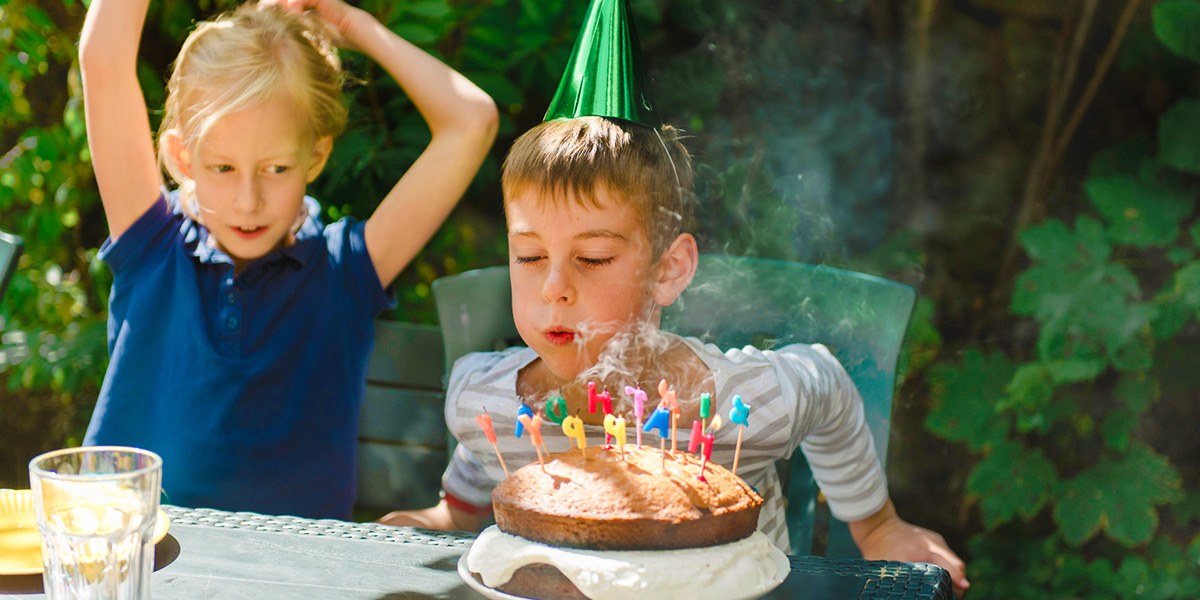 Ein Junge pustet die Kerzen auf seiner Geburtstagstorte aus – als Inspiration für posterXXL Kinderparty Ideen und eine unvergessliche Kinderparty.