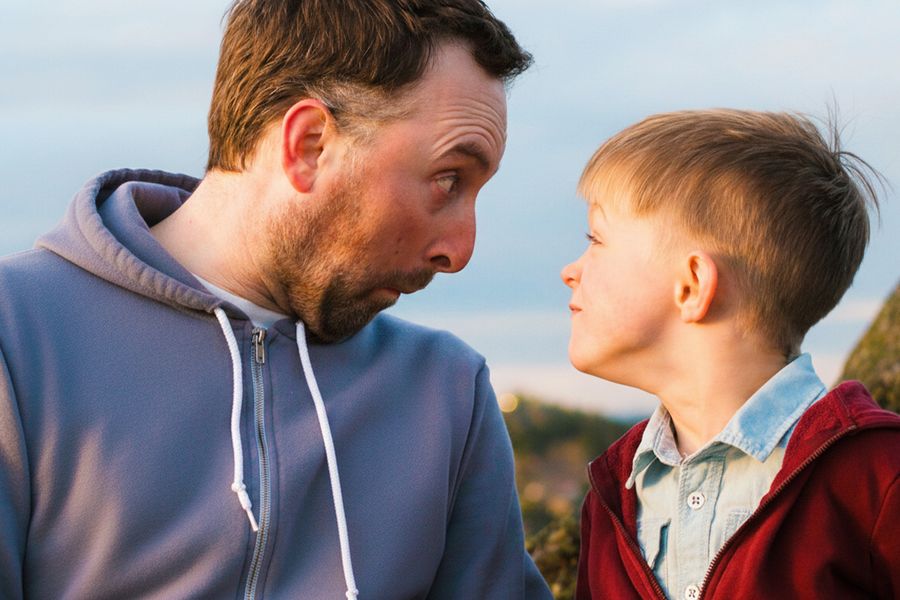 Ein Vater und sein Sohn schneiden Grimassen und schauen sich dabei an – als Inspiration für lustige Vatertagskarten und was man in eine Vatertagskarte schreiben kann.