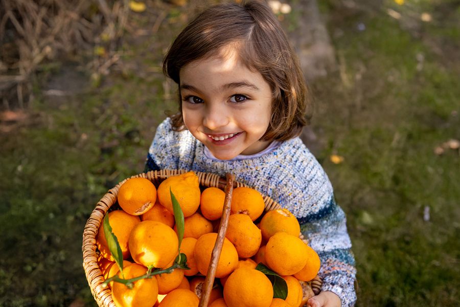 Ein junges Mädchen steht in hellem Sonnenlicht und hält eine Schale mit Orangen – als Beispiel für die Herausforderung, in der Mittagssonne zu fotografieren.