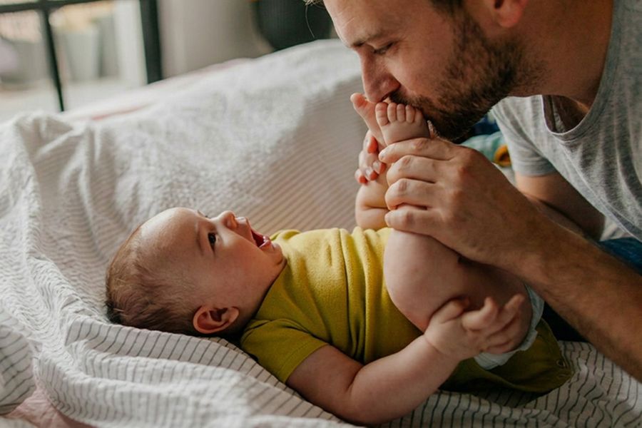 Ein Vater küsst die Füße seines Babys – als Inspiration für eine erste Vatertagskarte, liebe Worte für die Vatertagskarte und einen besonderen ersten Vatertag.