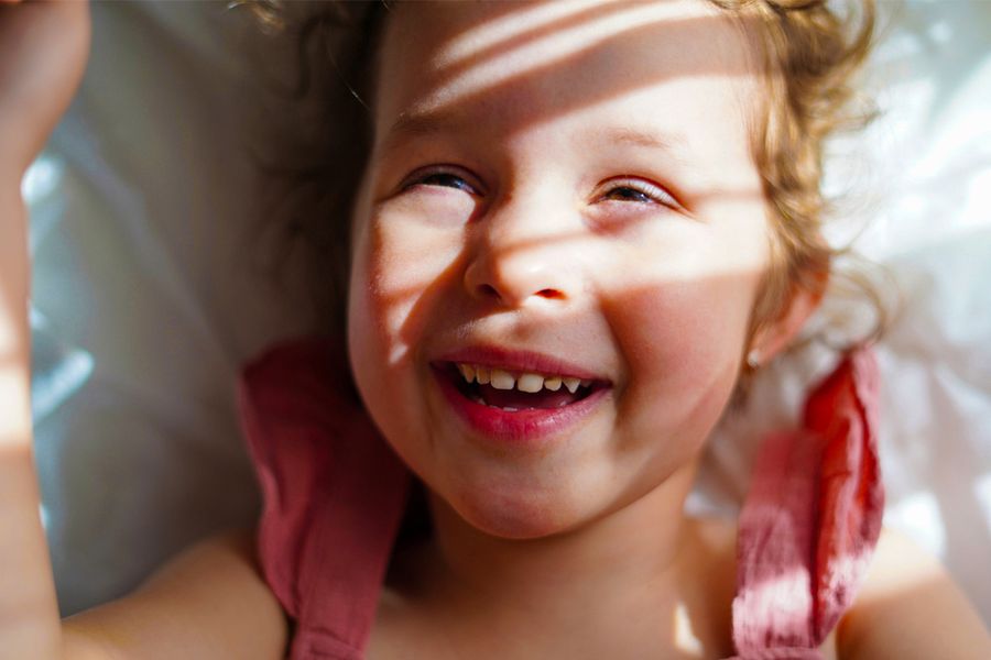 Ein lächelndes kleines Mädchen mit Sonnenlicht und weichen Schatten im Gesicht – als Inspiration für posterXXL Tipps, wie man gute Fotos bei hellem Sonnenlicht macht.