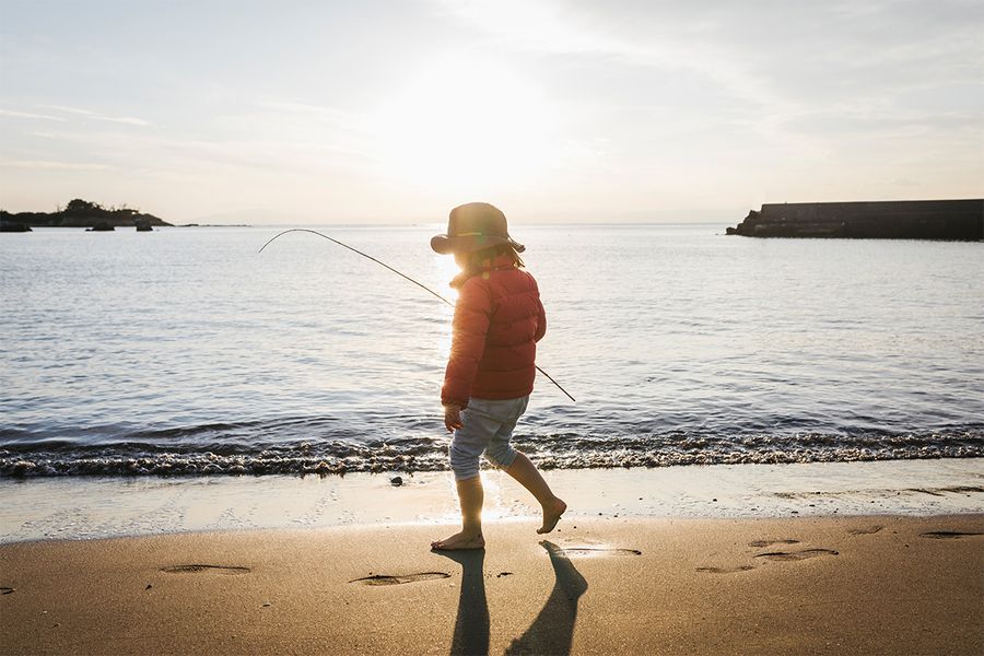 Ein Kind steht am Strand direkt am Meer, mit einem deutlichen Schatten hinter sich – als Beispiel für den dramatischen Effekt von Silhouettenfotografie im Sonnenlicht.