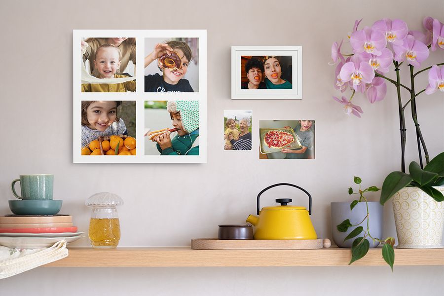 Ein Holzregal mit wohnlichen Deko-Elementen steht unter einer personalisierten Fotocollage mit Kindern, einem gerahmten lustigen Fotoabzug und zwei weiteren Familienfotos an der Wand – eine kreative Idee für Fotodrucke an der Wand.