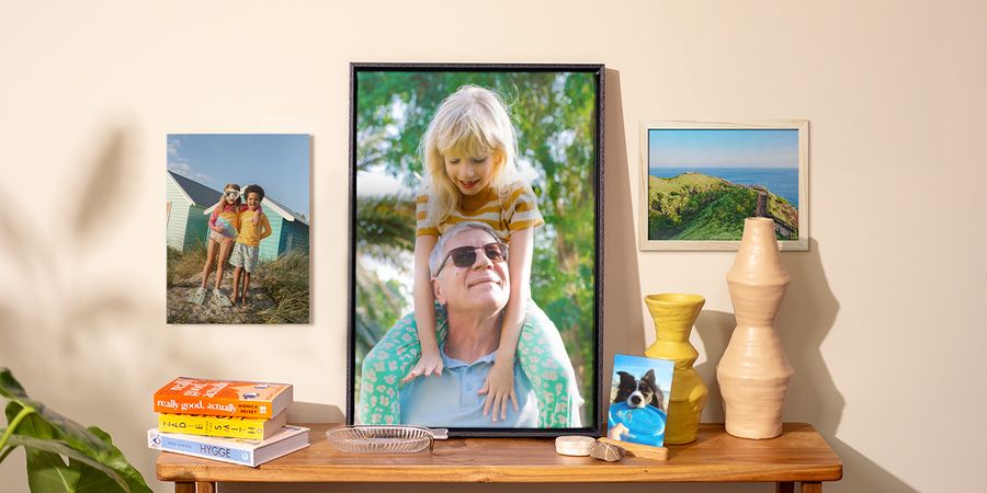 Eine Auswahl an posterXXL Fotoabzügen im Zuhause, darunter ein Hundefoto auf einem Beistelltisch, ein Poster mit Kindern an der Wand und zwei gerahmte Fotos – als Inspiration für Fotodrucke an der Wand und frische Frühlingsdeko.