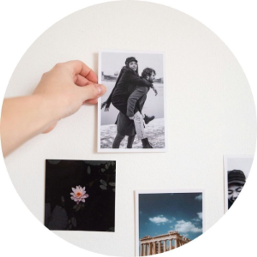 Eine Hand hält einen Fotoabzug eines Paares neben weiteren Fotoabzügen, als Illustration von Andreas Verlobungsgeschichte und einer bedeutungsvollen Heiratsantrag-Idee voller Erinnerungen von posterXXL.