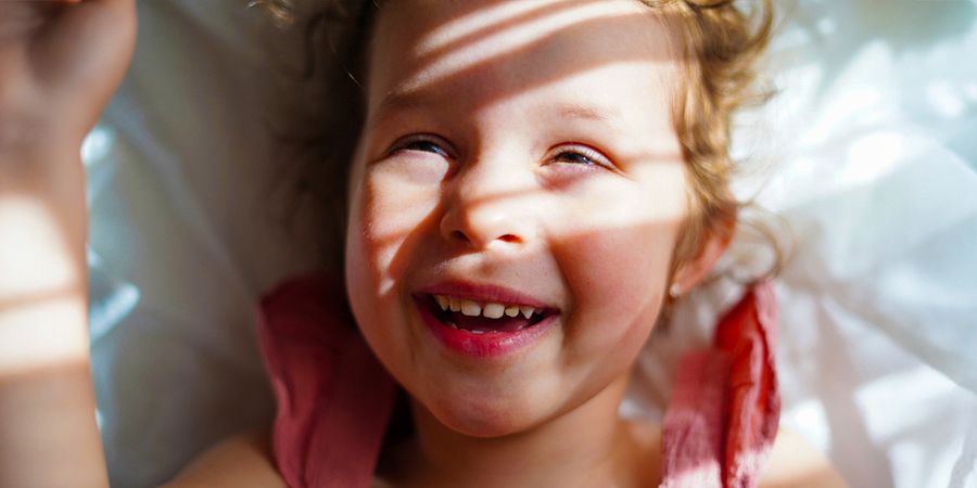 Ein lächelndes kleines Mädchen mit Sonnenlicht und weichen Schatten im Gesicht – als Inspiration für posterXXL Tipps, wie man gute Fotos bei hellem Sonnenlicht macht.