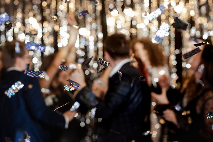 Konfetti fliegt durch den Ballsaal, während unscharfe Gäste im Hintergrund für eine kreative und festliche Abiball-Stimmung sorgen