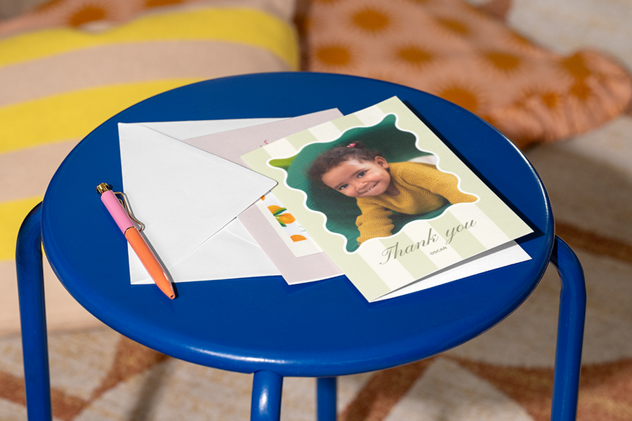 Eine personalisierte posterXXL Dankeskarte für Lehrer mit dem Foto eines kleinen Mädchens auf der Vorderseite liegt auf einem Hocker, daneben ein Stift – als Inspiration für einen warmen und respektvollen Text in einer Dankeskarte für Lehrer.