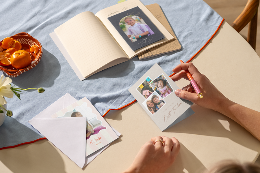 Die Hand einer Frau liegt auf einem Tisch und ist bereit, in eine personalisierte posterXXL Dankeskarte für Lehrer zu schreiben, die mehrere Fotos fröhlicher Kinder zeigt.