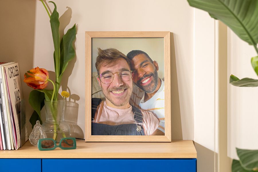 Ein gerahmtes Foto von zwei Männern, die in der Sonne ein Selfie machen, steht auf einem Sideboard neben einer Vase, einer Sonnenbrille und einer Zeitschrift – als Inspiration für sommerliche Deko Ideen im Wohnzimmer.