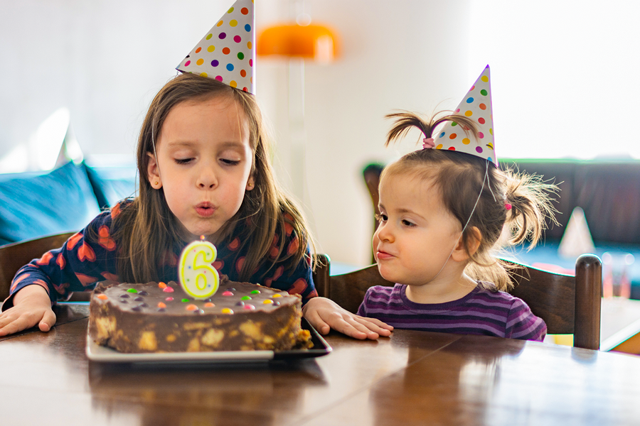 Ein Mädchen mit Partyhut pustet die Kerze auf ihrem Kuchen zum 6. Geburtstag aus; ein passendes Bild für ein personalisiertes Geburtstagsgeschenk von posterXXL.