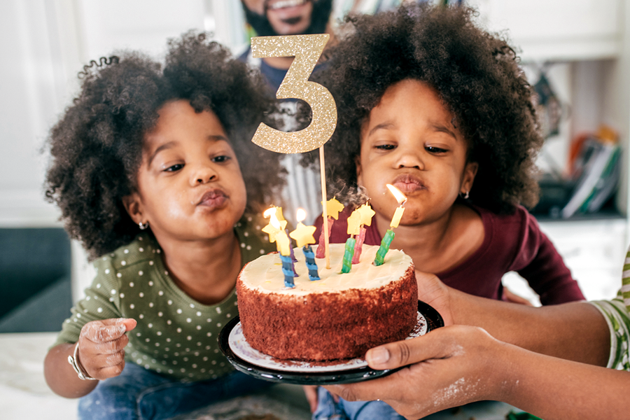 Zwei Zwillingsmädchen, die kurz davor sind, die Kerzen auf ihrem Kuchen zum 3. Geburtstag auszupusten; ein tolles Motiv für ein personalisiertes Geburtstagsgeschenk von posterXXL.