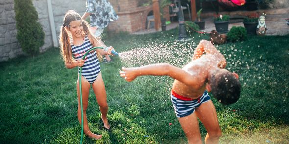 Ein Mädchen und ein Junge spielen im Garten mit einem Gartenschlauch, ein fröhlicher Staycation-Moment aus dem posterXXL-Ratgeber zur Planung der perfekten Staycation.