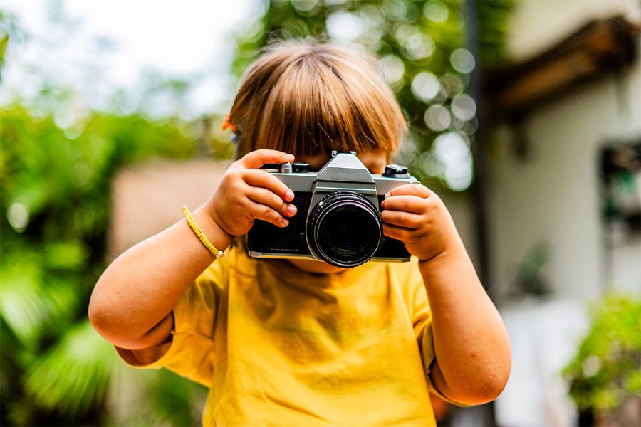 Ein junges Mädchen macht Fotos mit einer Kamera, was posterXXLs kreative Staycation-Ideen widerspiegelt.