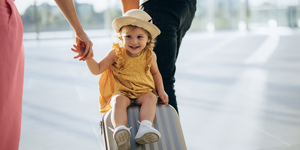 Ein kleines Mädchen sitzt auf einem Koffer, der gezogen wird, und das Bild zeigt einen verspielten Moment aus dem Familienurlaub und Reisen mit der Familie mit posterXXL.