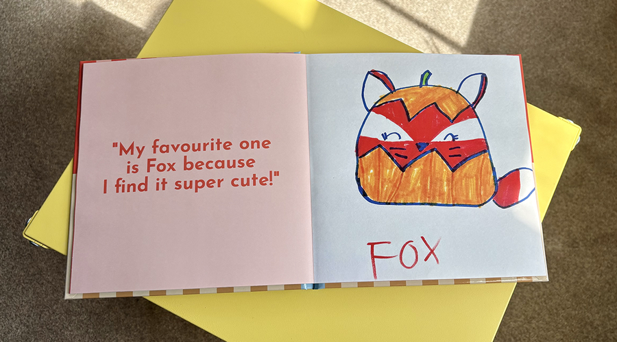 Ein aufgeschlagenes Kinderfotobuch zeigt links eine Bildunterschrift und ein Zitat eines Mädchens, das ihr Kunstwerk erklärt, daneben ihre dazugehörige Zeichnung eines Cartoon-Fuchses rechts, und veranschaulicht posterXXLs Tipps zum Hinzufügen von Text zu einem Kinderfotobuch.