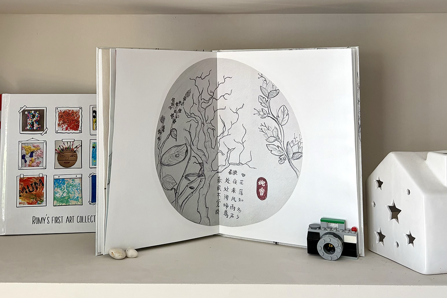 Ein aufgeschlagenes Kinderfotobuch zeigt eine doppelseitige Baumzeichnungsseite mit Text, neben einem geschlossenen Fotobuch mit einem Scrapbook-artigen Cover mit verschiedenen Beispielen von Kinderkunst, das das bedeutungsvolle Andenken veranschaulicht, das ein posterXXL Kinderfotobuch schafft.