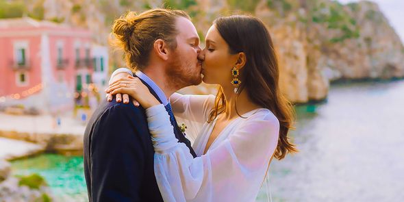 Eine Braut und ein Bräutigam küssen sich an ihrem Hochzeitstag vor einer mediterranen Kulisse und spiegeln damit hochzeitstrends 2026 sowie eine personalisierte Hochzeit von posterXXL wider.