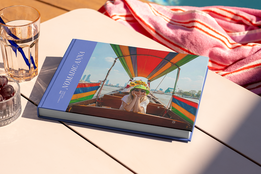 Ein großes querformatiges Reisefotobuch mit dem Titel 'Nomadic Anna' liegt auf einem Tisch, mit einem Foto eines Mädchens auf Reisen auf dem Cover, und veranschaulicht posterXXLs Fotobuch Titel Ideen für Reisen.
