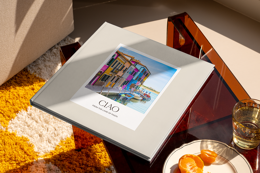Ein Fotobuch mit einem Kanal und bunten Häusern in Italien auf dem Cover trägt den Titel 'Ciao from the Land of Pasta', und veranschaulicht posterXXLs Fotobuch Titel Ideen für Städtereisen.