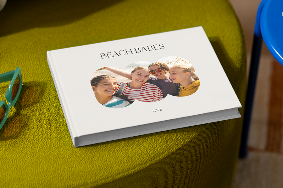 Ein Fotobuch mit vier lächelnden Mädchen auf dem Cover trägt den Titel 'Beach Babes', und veranschaulicht posterXXLs Fotobuch Titel Ideen für Reisen mit Freunden.