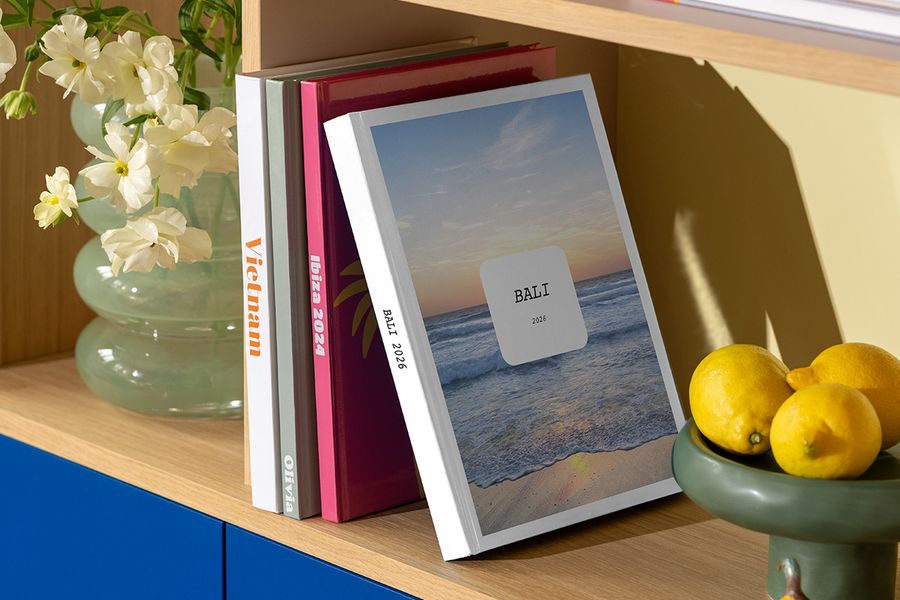 Das neue Modern Travelogue Fotobuch von posterXXL steht auf einem Regal, mit klaren Layouts und eleganter Typografie, inspiriert von Reisemagazinen und Coffee-Table-Books.