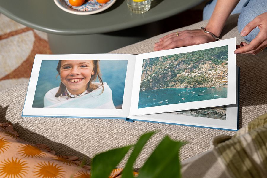 Ein aufgeschlagenes Fotobuch zeigt auf einer Seite ein lächelndes Mädchen am Meer und auf der anderen eine Strandlandschaft, und veranschaulicht posterXXLs Holiday Escape-Design mit eindrucksvollen ganzseitigen Fotografien.