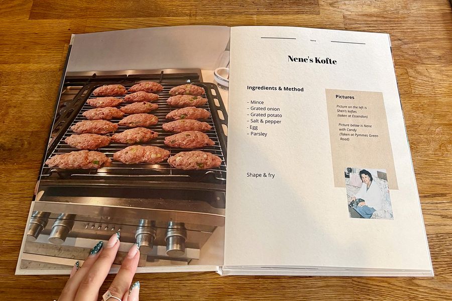Eine aufgeschlagene Doppelseite aus Sarahs Rezeptbuch zeigt Nenes Kofte-Rezept, mit einer manikürten Frauenhand, die auf dem Buch auf einer Holztheke ruht, und veranschaulicht posterXXLs letzte Checklisten-Tipps vor dem Drucken eines persönlichen Kochbuchs.